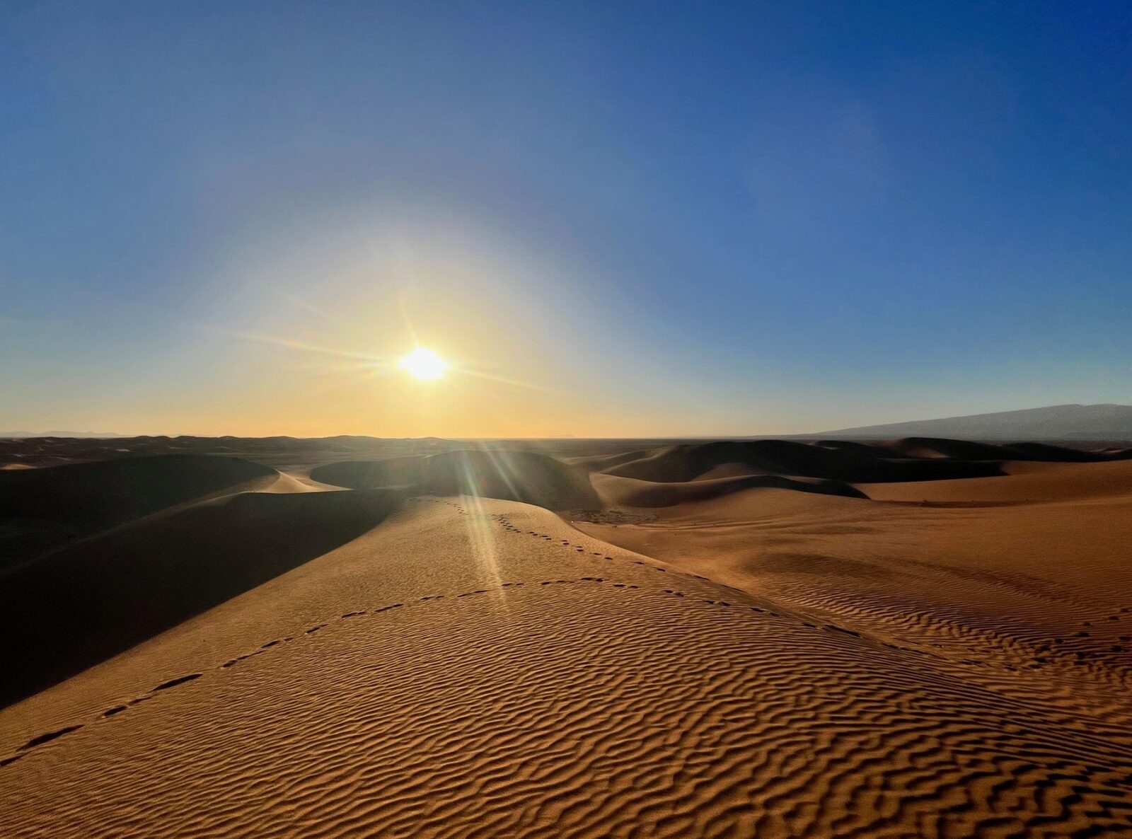 Sanddünen der Sahara, blauer Himmel, Sonne kurz über Horizont