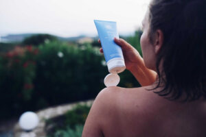 Frau in Rüeckenansicht mit Speick Sun After Sun flege in blauer Tube vor grüner Landschaft