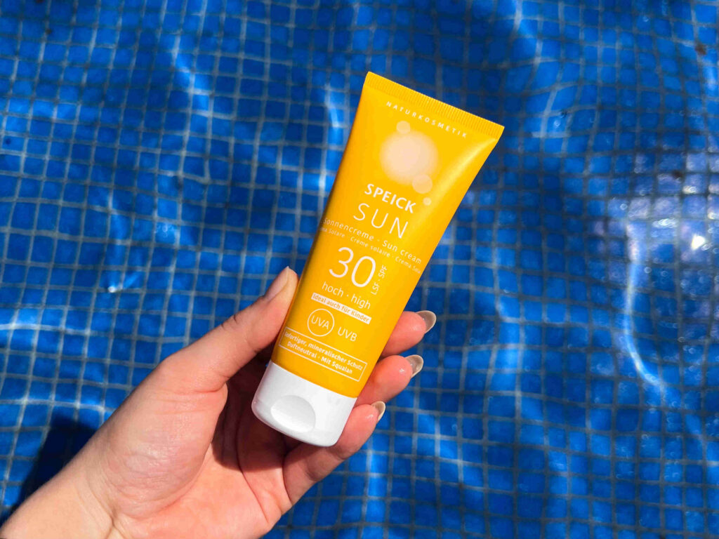 Speick Sun: Hand mit gelber Tube mit blauem Pool im Hintergrund