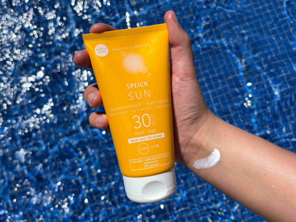 Speick Sun: Eine Hand mit gelber Tube und blauem Pool im Hintergrund