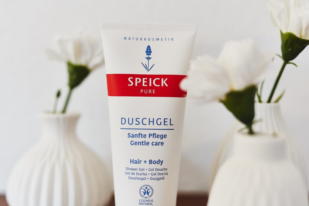 Eine Tube Speick Pure Duschgel zwischen zwei weißen Vasen mit Blüten